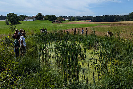 Eine Gruppe Menschen steht an einem Gewässer.